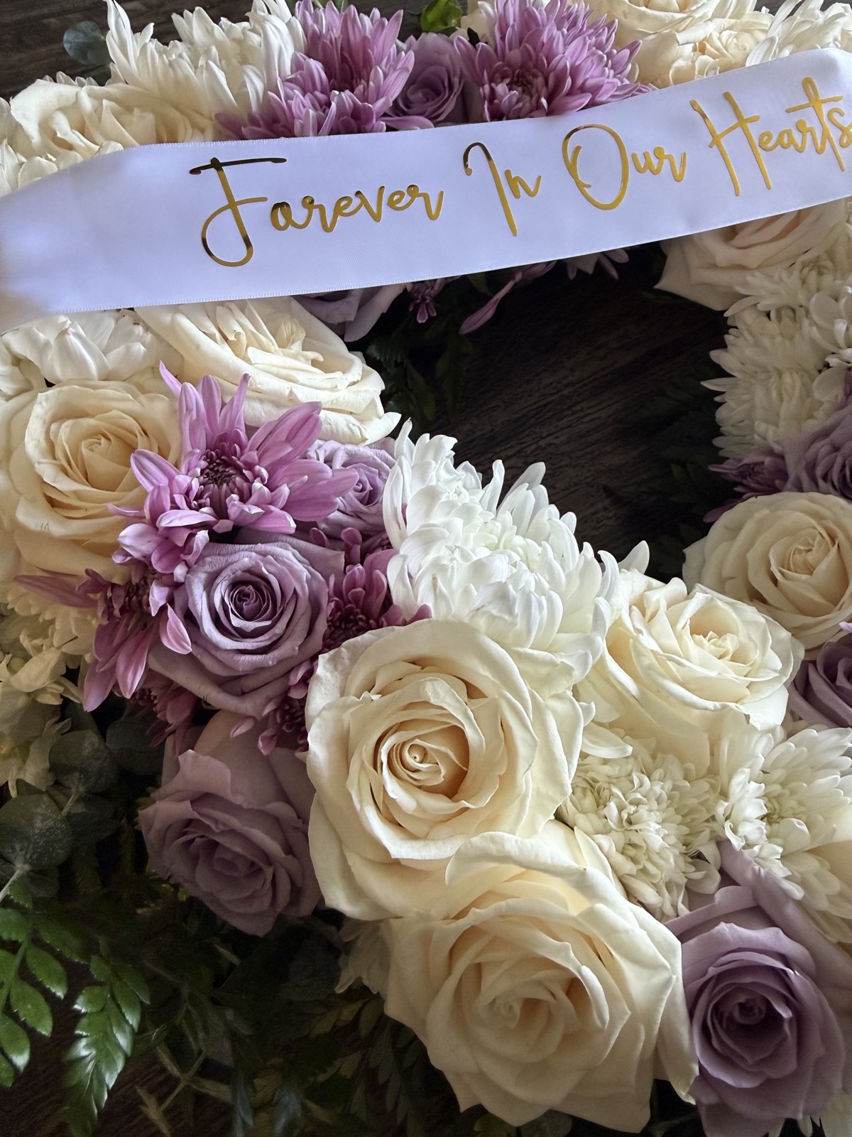 Close-up detail of a sympathy wreath with cream roses, lavender roses, and a gold-lettered satin sash